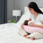 New mom breastfeeding baby on Momcozy Original Nursing Pillow in cradle position