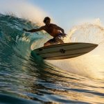 Surfer riding wave on eco-friendly surfboard made from sustainable materials in clear blue ocean water